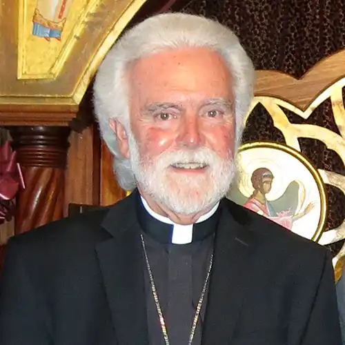 An older Caucasian man with white hair and beard wearing a clerical collar