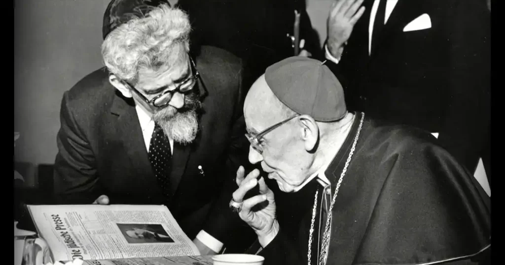 Black-and-white image from 1965 of Rabbi Abraham Heschel leaning over a desk where Pope Paul VI is seated. They are signing the Nostra Aetate.