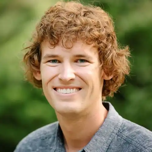 A Caucasian man in his late 20s with medium-brown curly hair