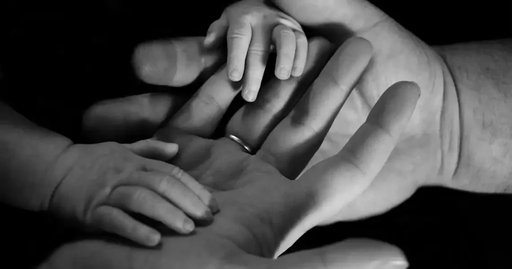 Black-and-white close-up of hands. One hand belongs to a woman, one to a man, and one to a baby