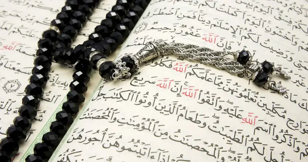 A close up of a page from the Qu'ran with prayer beads laid on top