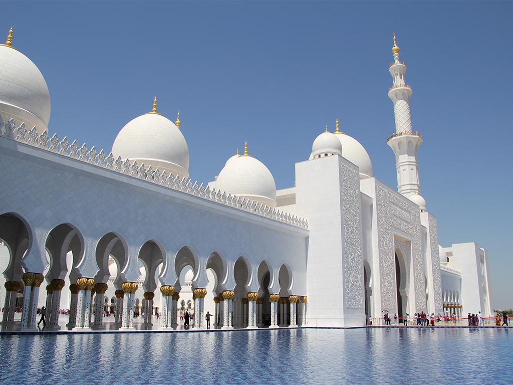 A white mosque with gold pillars and a gold spire seen against a blue sky