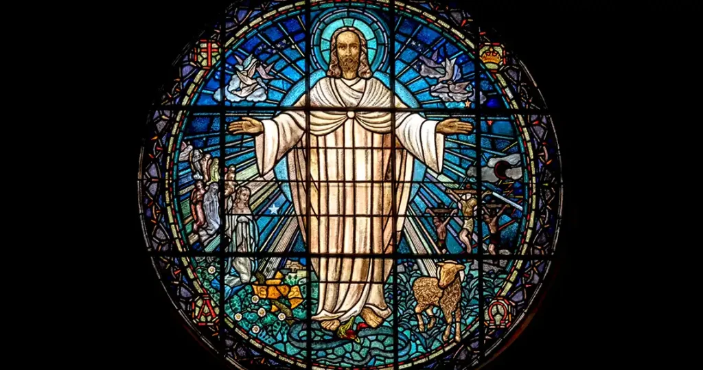A round stained glass window depicting Jesus surrounded by a meadow and a lamb