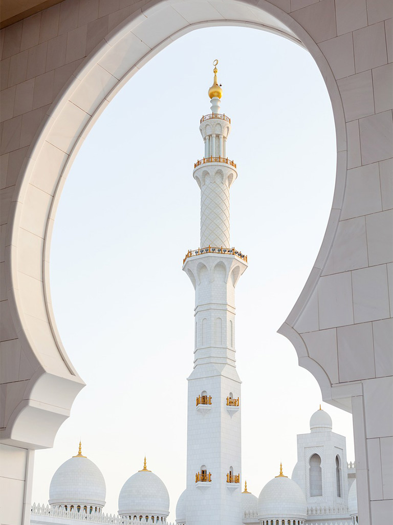 A gold and white pillar of the white mosque seen through a shaped arch